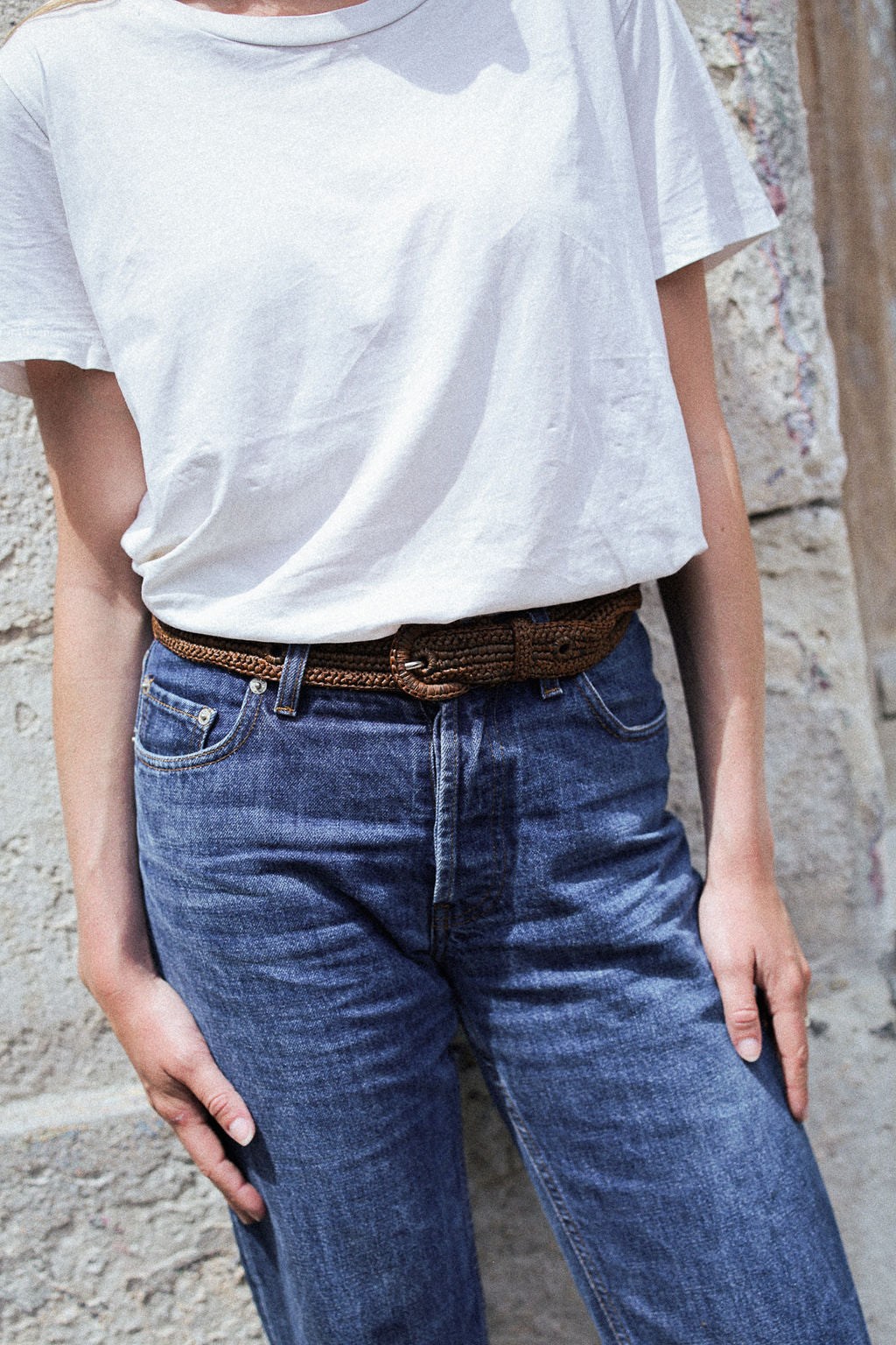 zoom sur la ceinture à boucle en raphia marron tabac portée sur un jean brut