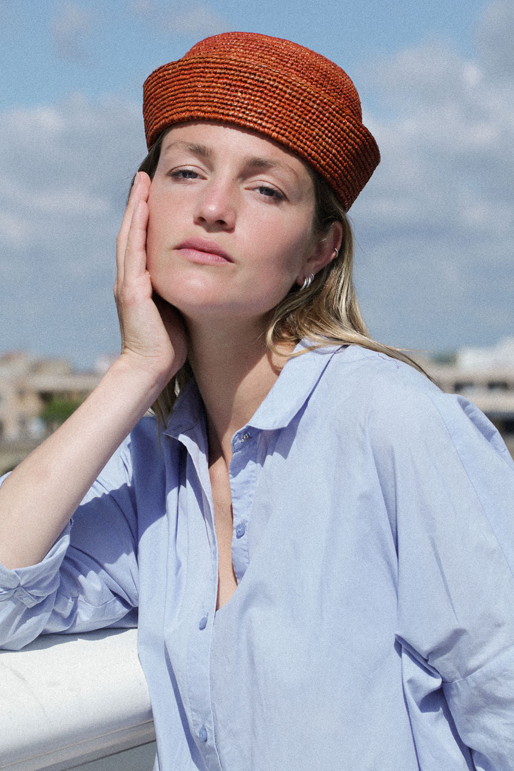 vue de face du petit chapeau en raphia terracotta porté avec une chemise bleue