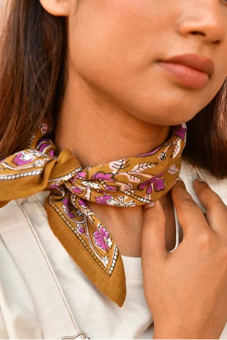 petit foulard en coton caramel aux motifs floraux violet et rose pâle noué au cou