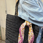 petit foulard en block print noué sur un sac en raphia noir 