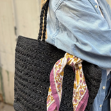 petit foulard en block print noué sur un sac en raphia noir 