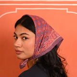 petit foulard en coton imprimé violet et rose noué sur la tête comme un fichu