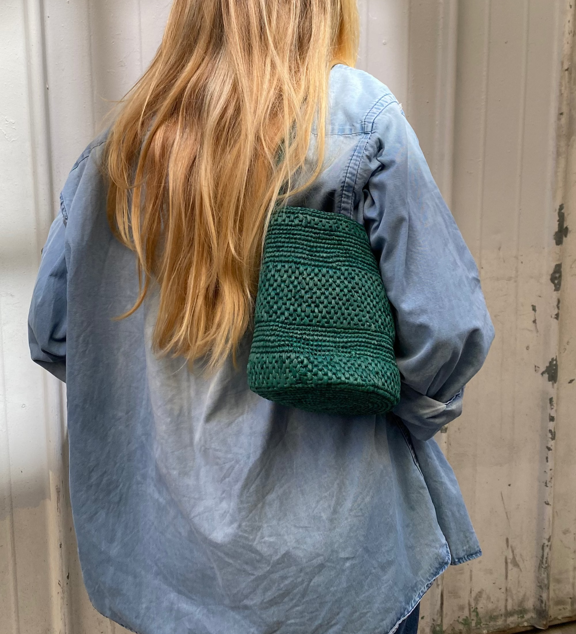 vue du dos du petit sac seau vert en raphia porté à l'épaule