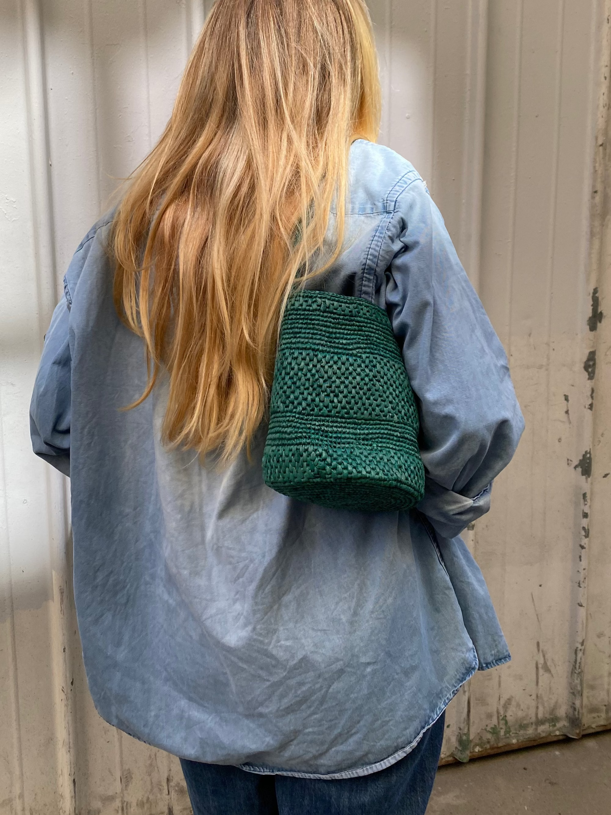 vue du dos du petit sac seau vert en raphia porté à l'épaule