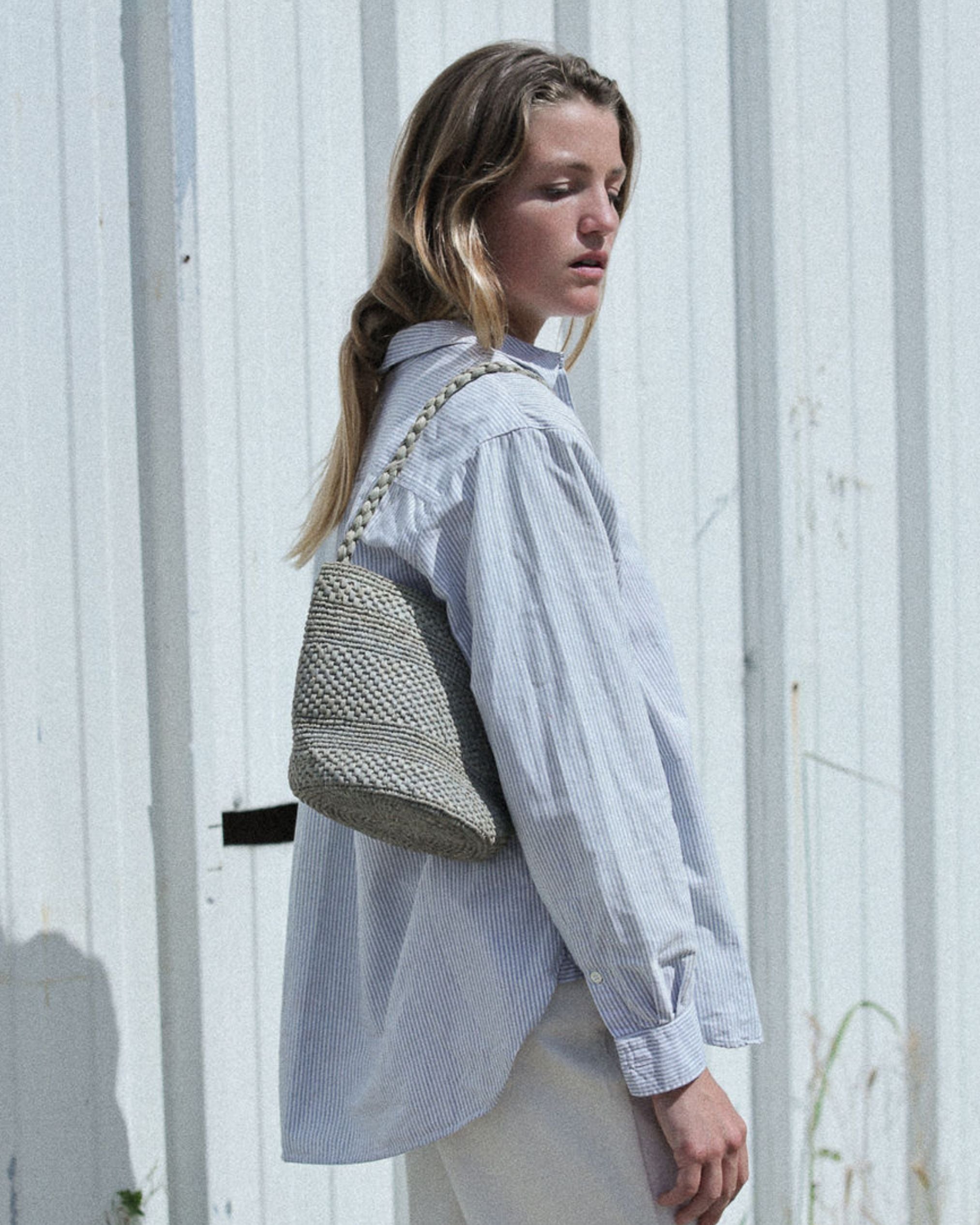 petit sac seau en raphia bleu gris porté à l'épaule