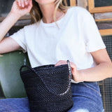 petit sac seau noir en raphia posé sur les jambes