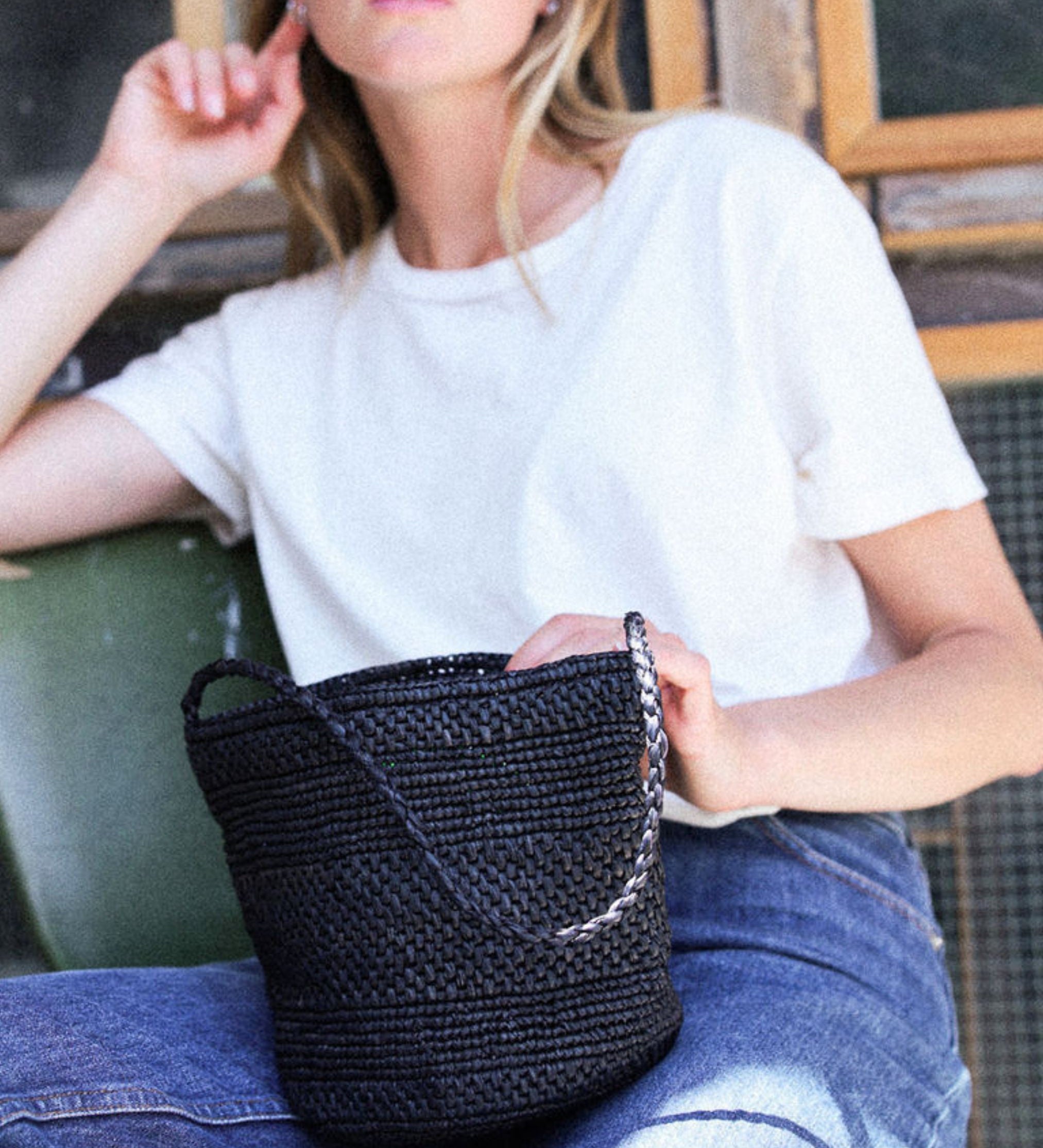 petit sac seau noir en raphia posé sur les jambes