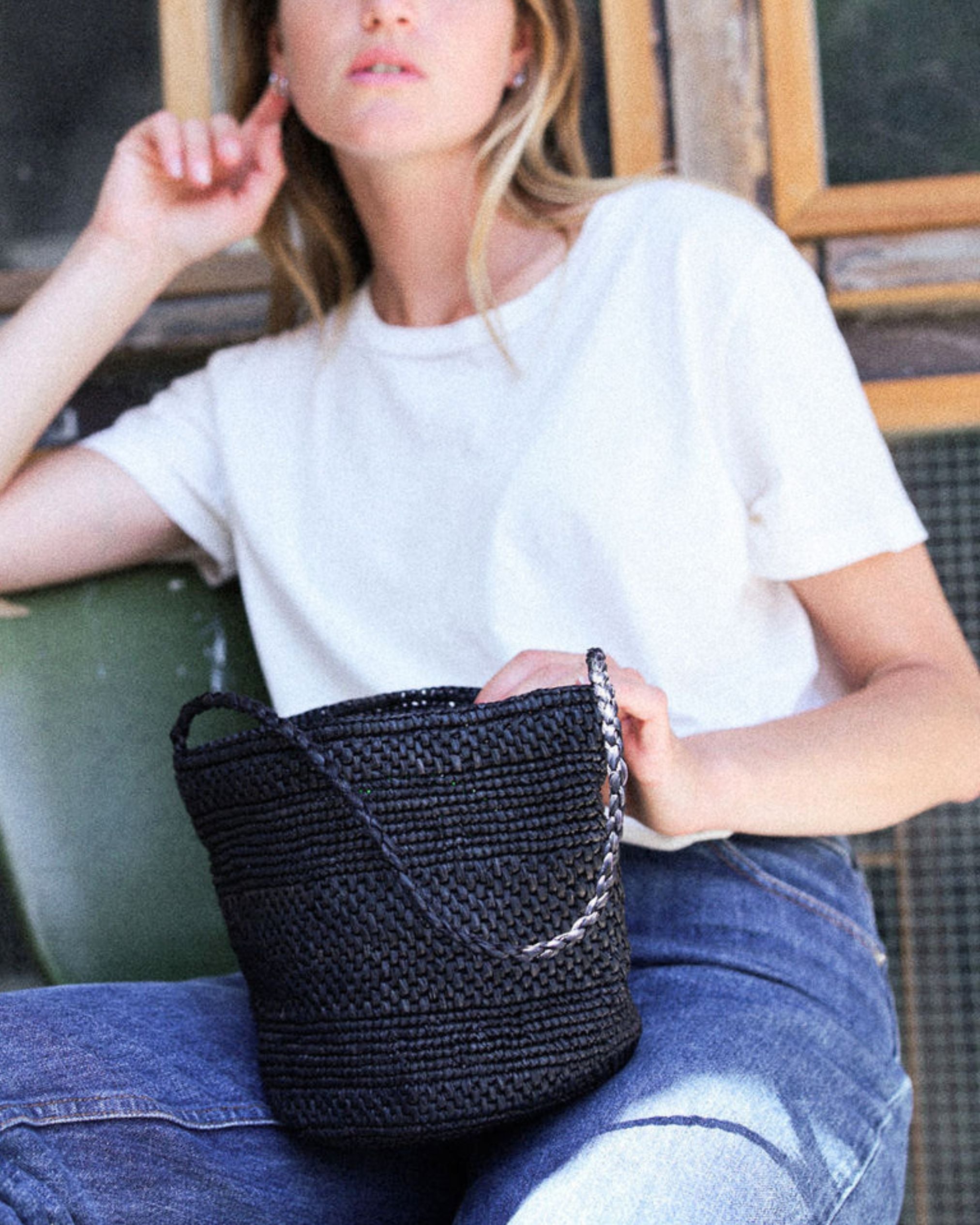 petit sac seau noir en raphia posé sur les jambes