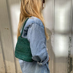vue de profil du petit sac seau vert en raphia porté à l'épaule