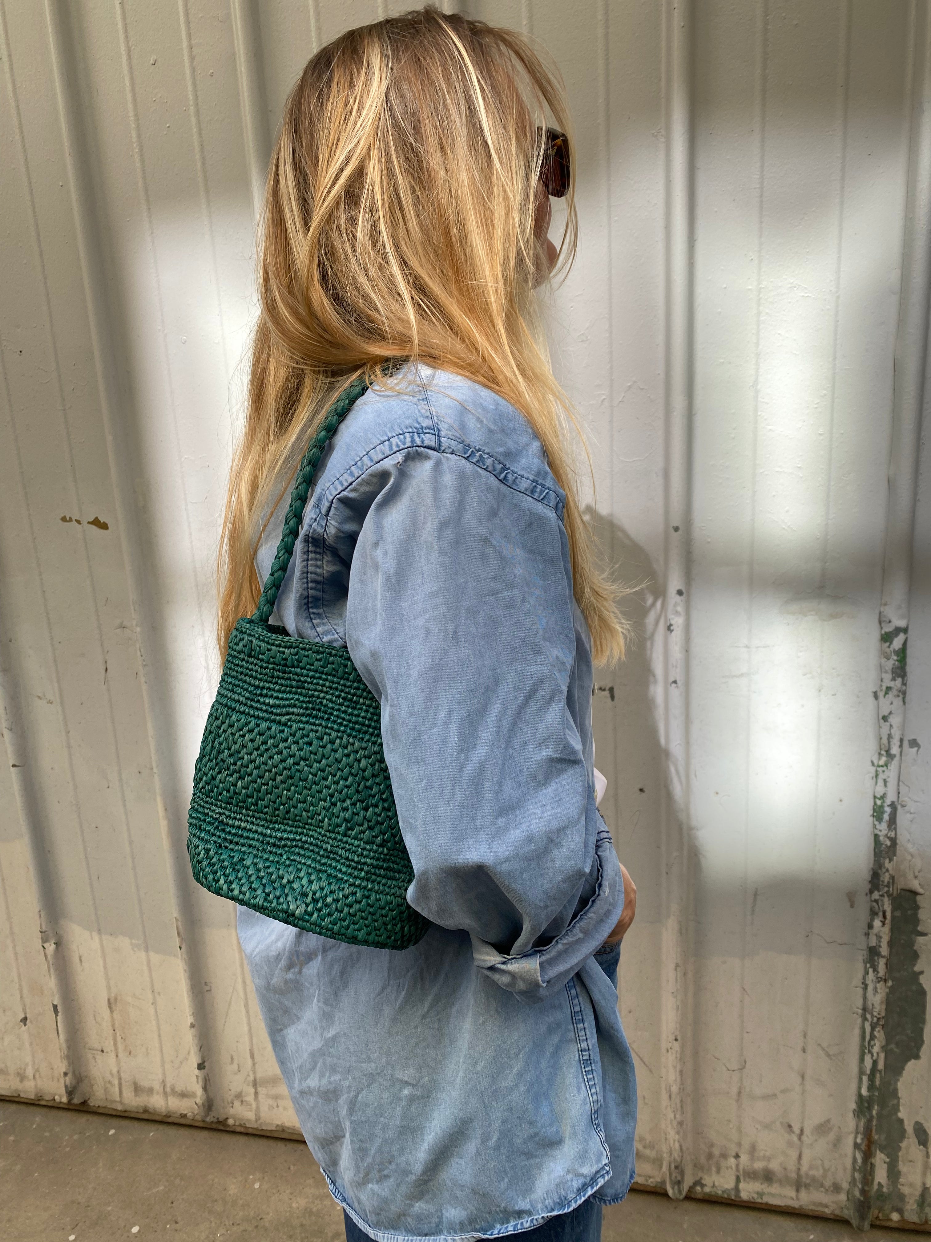 vue de profil du petit sac seau vert en raphia porté à l'épaule